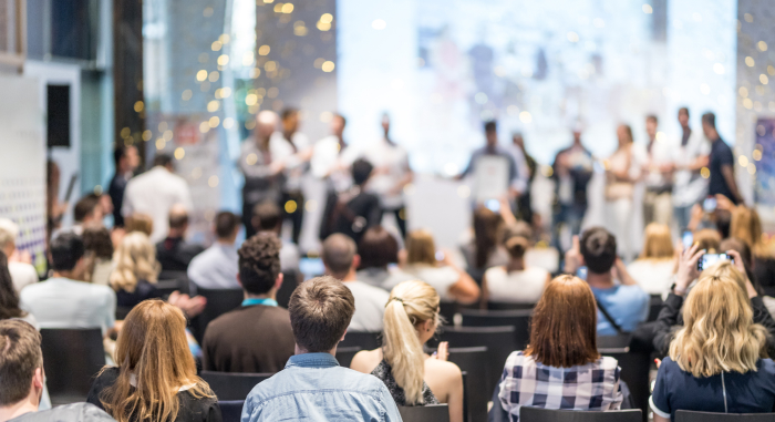 A crowd watching a presentation taking place on a stage.